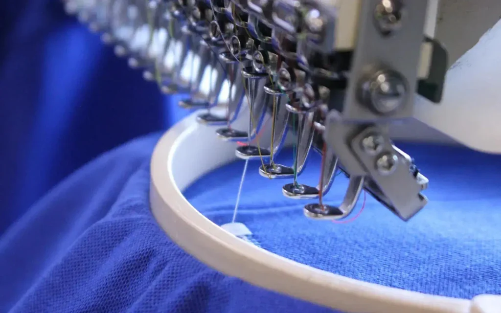 Close-up of an embroidery machine stitching fabric during the custom apparel production process.